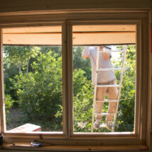 man on a ladder outside the window of the tiny house